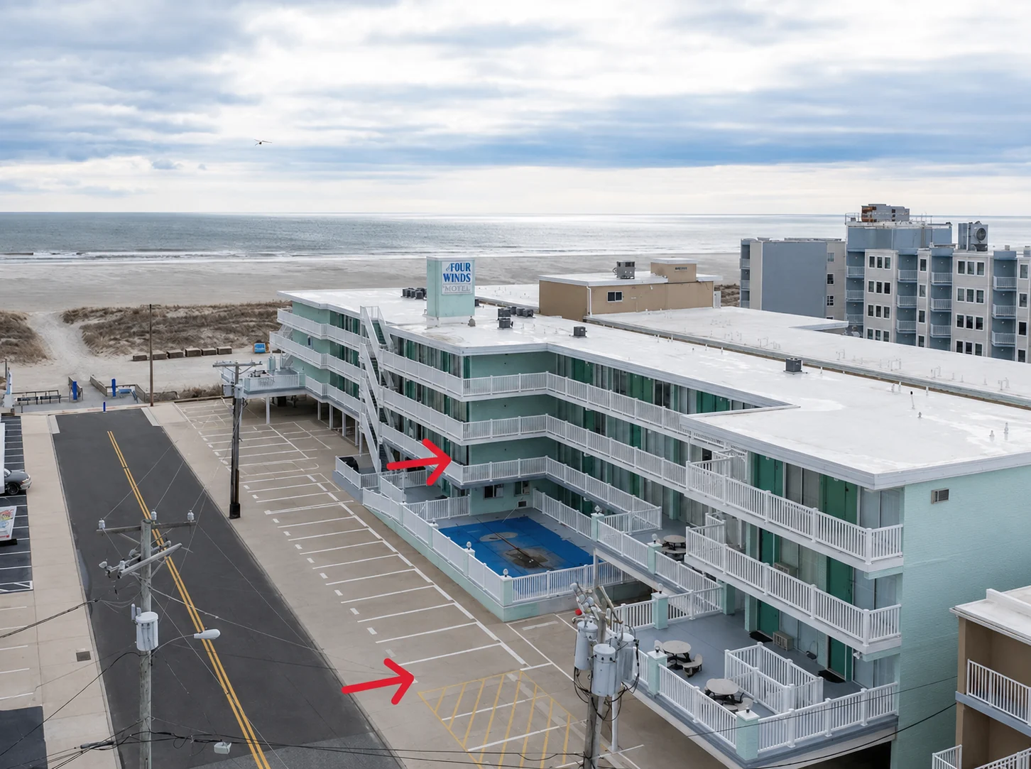 Aerial exterior photo of Four Winds on the Beach with red arrows marking Unit 210 and the designated parking area, with the pool and ocean visible